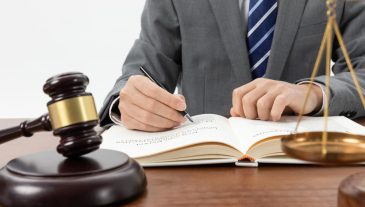 closeup-shot-person-writing-book-with-gavel-table