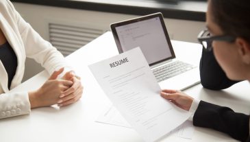 Company CEO and HR manager reading applicant resume or cv while employee waiting for questions, discussion and result during recruitment process in office. Concept of hiring, employment. Close up view