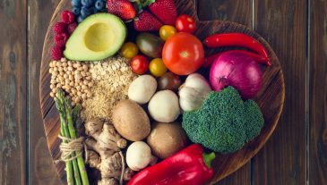 Healthy food on a heart shape cutting board. Love of food concept with fruit, vegetables, grains and high fibre foods. Rustic wood textures