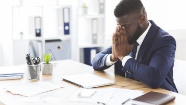 Young tired african american businessman having stress at work, sitting with closed eyes at workplace, empty space